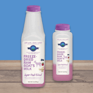 Two bottles of raw goat's milk with purple caps on a blue surface.